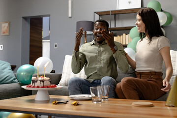 Surprised by birthday cake, African American man celebrates with smiling woman at home