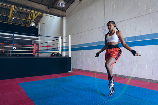 Jump rope swinging inside boxing gym, with white brick walls, red and blue ring nearby