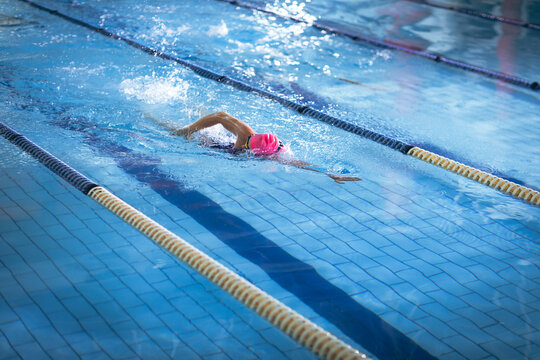 Swimmer is swimming in lane, with pink cap, goggles, swimsuit, yellow-black ropes and tiled bottom