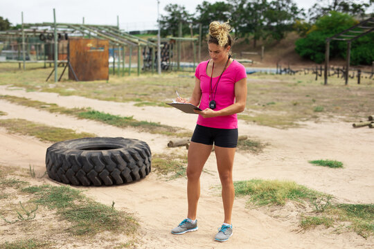 Holding clipboard, woman timing obstacle run at outdoor fitness course, with stopwatch lanyard - Powered by Adobe