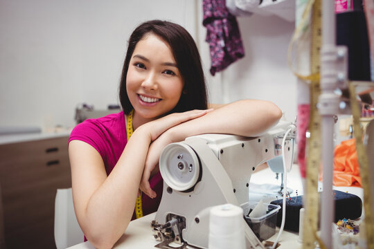Leaning woman in her twenties sewing on industrial sewing machine in workshop, with tape measure