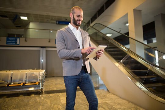Smiling businessman tapping tablet computer at spacious modern airport concourse, copy space