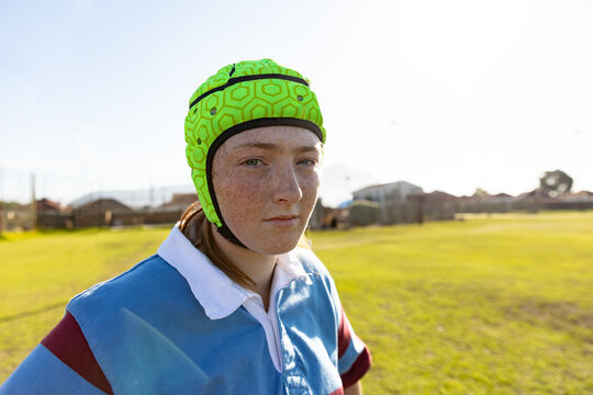 Teenage girl standing on grassy sports field in suburb, with helmet and jersey, copy space