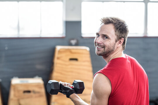Smiling mid adult man holding hexagonal dumbbell in gym, with wooden plyometric boxes, copy space