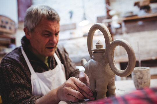 Clay teapot sculpture taking shape on wooden worktable in pottery workshop, under warm lighting