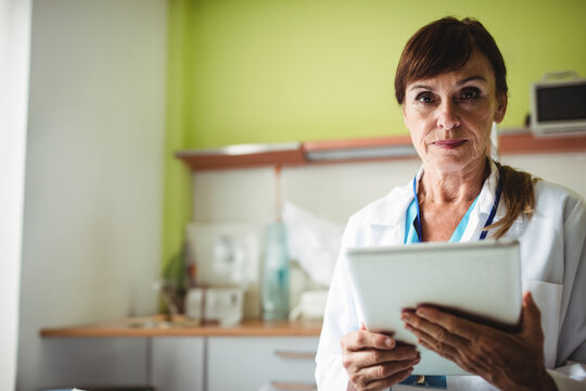 Senior doctor is holding tablet in medical consultation room, highlighting stethoscope and supplies