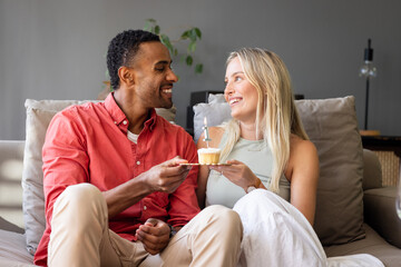 Celebrating with cupcake, couple smiling on couch, sharing special moment together