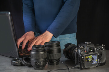 Photographer working on laptop with multiple camera lenses and DSLR preparing for upcoming project at home