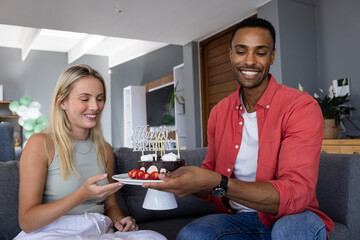 Smiling friends celebrating birthday at home, sharing cake and enjoying together