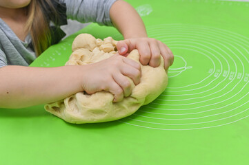 Child baker learning on kitchen table. Messy fun kitchen moment capturing childhood cooking curiosity. Little girl happily mixes dough