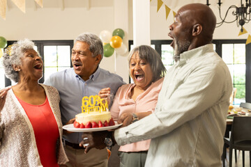 Celebrating 60th birthday, joyful friends laughing and holding cake indoors