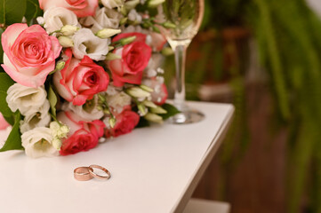 Love expressed through wedding rings, fresh roses, and champagne glass on table. Table top with rings, bouquet, and champagne marks meaningful moment. Wedding symbols concept of love, wedding card.