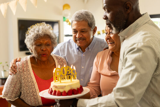Elderly woman surrounded by family blowing out candles on birthday cake - Powered by Adobe