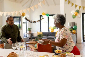 Elderly couple preparing for celebration, arranging dishes and decorations at home