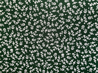 Fabric with seamless vintage small floral pattern, close-up as texture. Old-fashioned, retro style cotton or linen textile with print of scattered small white flowers on green background