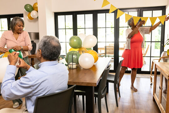 Senior friends hanging bunting and arranging balloons for celebration at home - Powered by Adobe