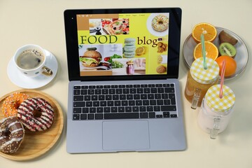 Laptop with food blog web site, different drinks, fruits and donuts on beige background, above view