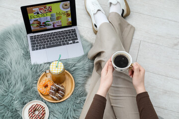 Blogger holding coffee near laptop with food blog web site on floor indoors, above view