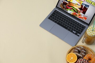 Laptop with food blog web site, juice, orange and donuts on beige background, above view. Space for...