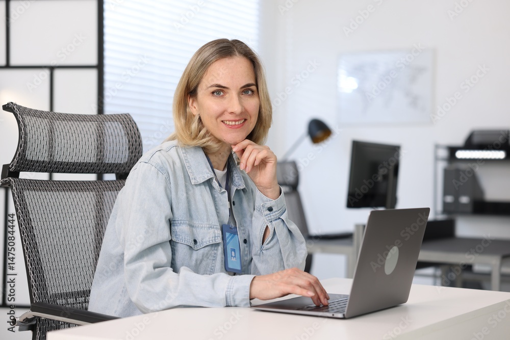 Poster smiling engineer working with laptop at table in office