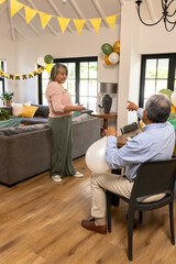 Obraz premium Smiling woman holding gift while man with balloons points in living room