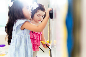 Two preschool girls drawing on whiteboard in kindergarten classroom