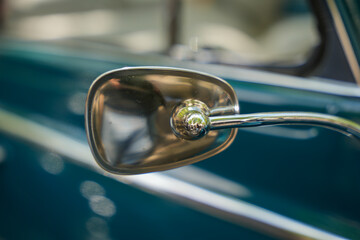Vintage side mirror on teal classic car. Close-up of a vintage-style, rounded side mirror on a...
