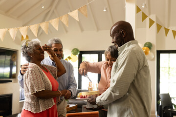 Celebrating birthday at home, elderly friends cutting cake and sharing joy