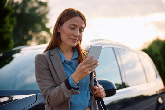 Smiling businesswoman using cell phone in front of her car.