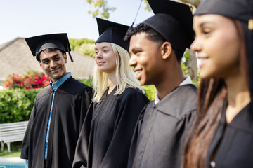 Graduating students in caps and gowns smiling outdoors, celebrating achievement