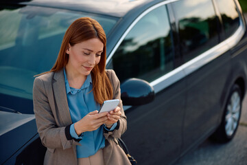 Happy businesswoman using cell phone while standing beside her car on parking lot.