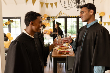 Graduates in caps and gowns celebrating with drinks at home party