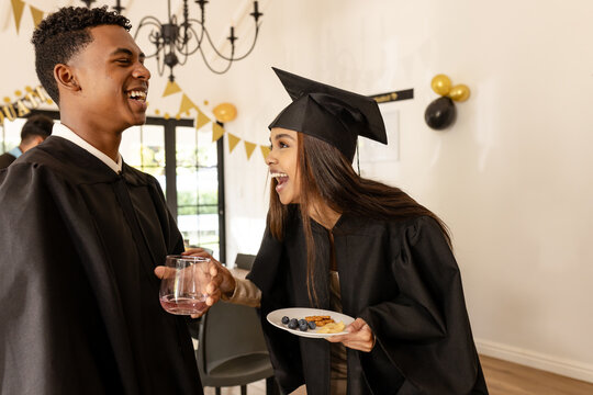 Graduates in caps and gowns celebrating with snacks and drinks at party