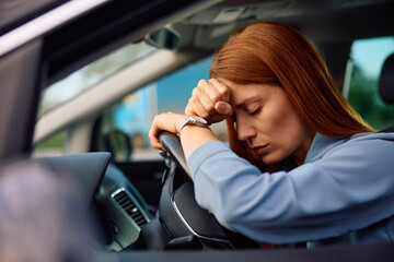 Exhausted businesswoman leaning on steering wheel while driving car.