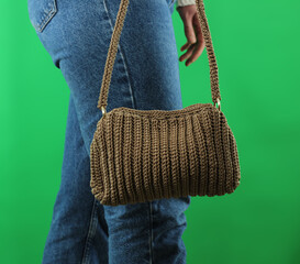 Woman with brown crochet bag hanging on arm in front of green background. World knitting day concept idea.
