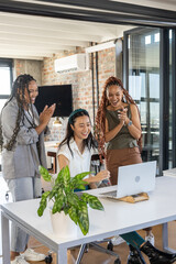 Team celebrating success at office, three women clapping and smiling at laptop