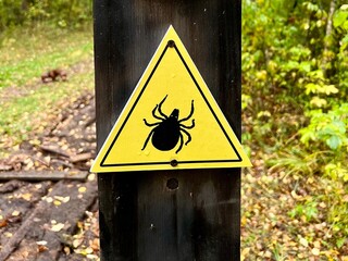 Photo of a yellow warning sign with a tick symbol. Caution about tick danger in forest areas. Ideal...