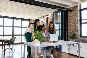 In office, colleagues sharing ideas enthusiastically while collaborating around laptop