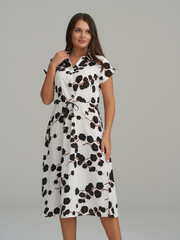Woman wearing a knee-length, floral-patterned dress with short sleeves and a tied waist. The dress...