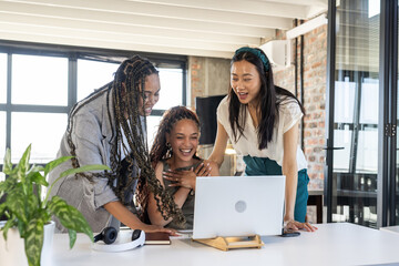 Colleagues celebrating success while looking at laptop in modern office