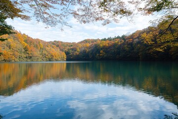 Serene autumn lake mirroring vibrant foliage-clad hills under a partly cloudy sky