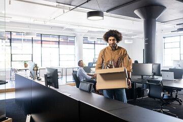 Man carrying box in modern office, preparing for new job transition