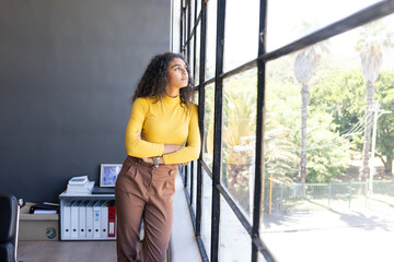 Gazing thoughtfully out office window, businesswoman in yellow sweater contemplating ideas