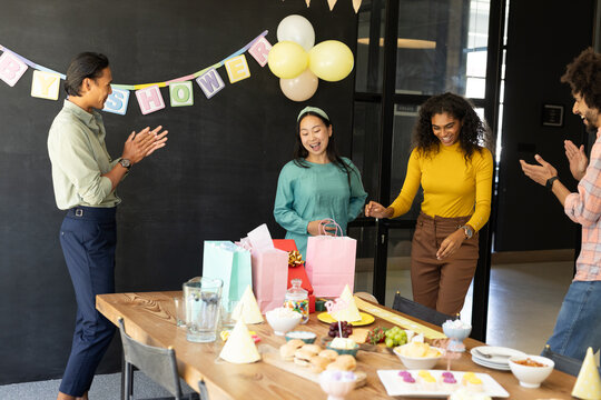 Colleagues celebrating baby shower in office, smiling and clapping around gift table