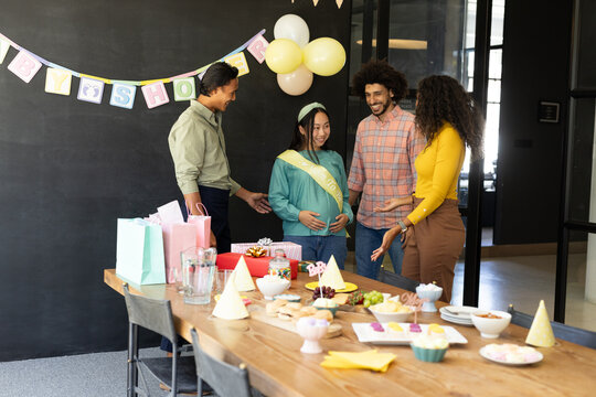 Celebrating baby shower, diverse friends congratulating expectant mother in office setting