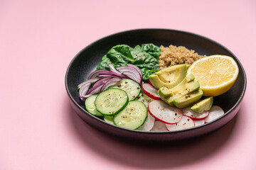 Quinoa, spinach, avocado, radish and lemon wedge vegan food. Healthy food in a bowl on a pink background with copy space.