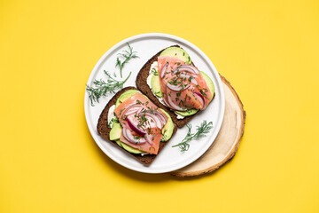 Smoked salmon avocado sandwich on yellow background. Black whole grain bread, avocado, salted salmon and dill for healthy breakfast
