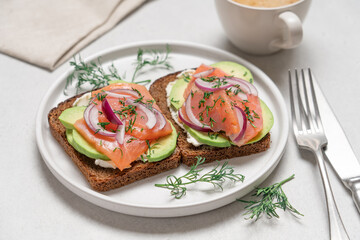 Smoked salmon avocado sandwich on light background. Black whole grain bread, avocado, salted salmon and dill for healthy breakfast