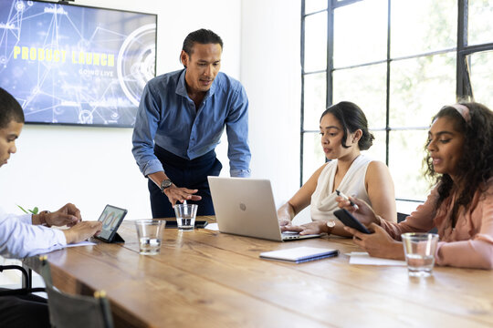 Business team collaborating on laptops and tablets during product launch meeting