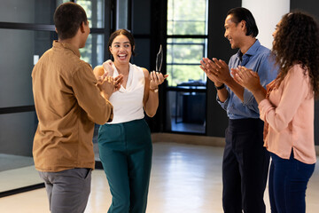 Business team celebrating colleague receiving award in modern office setting